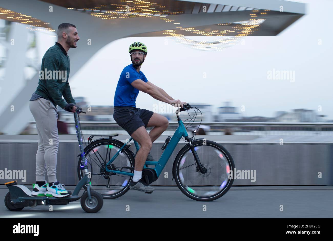 Männer reiten Roller und Fahrrad entlang der städtischen Uferpromenade Stockfoto