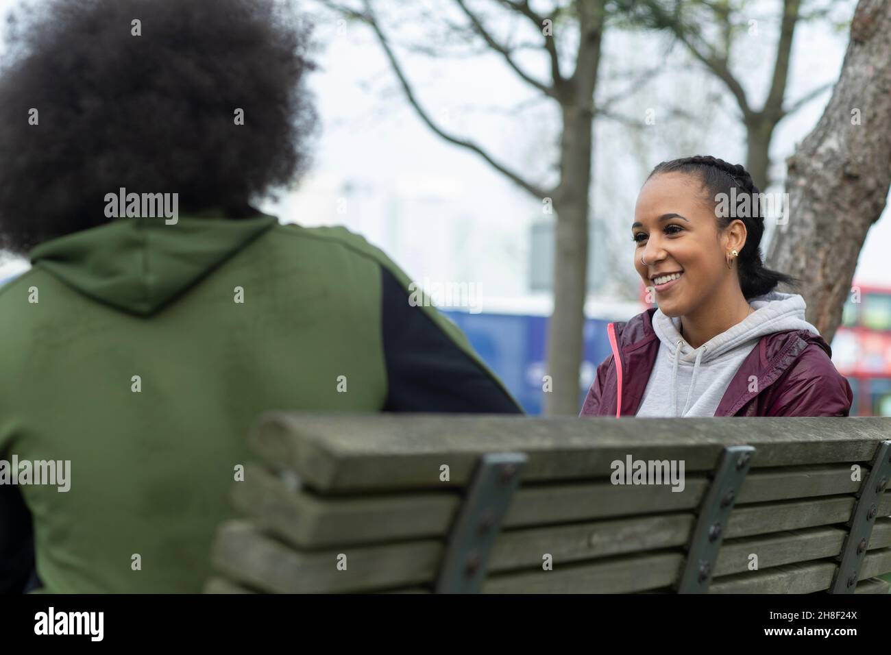Glückliche junge Frau im Gespräch mit einem Freund auf der Parkbank Stockfoto
