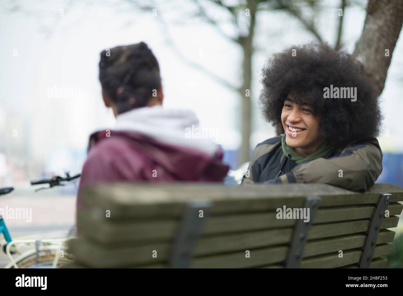 Glücklicher junger Mann mit Afro im Gespräch mit einem Freund auf der Parkbank Stockfoto
