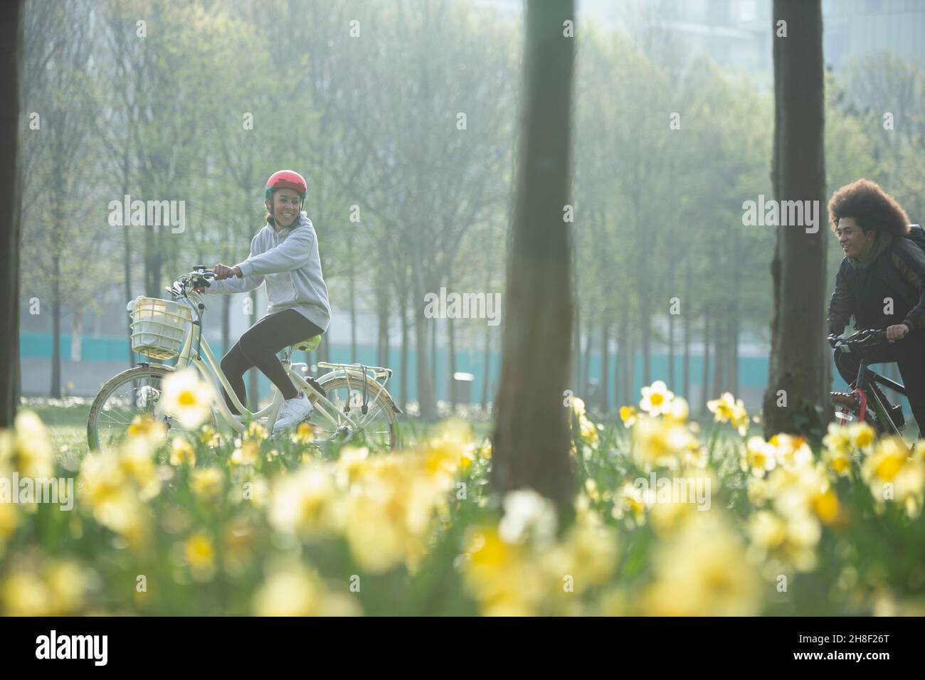 Glückliche Teenager-Freunde, die im sonnigen Frühlingspark Fahrräder reiten Stockfoto