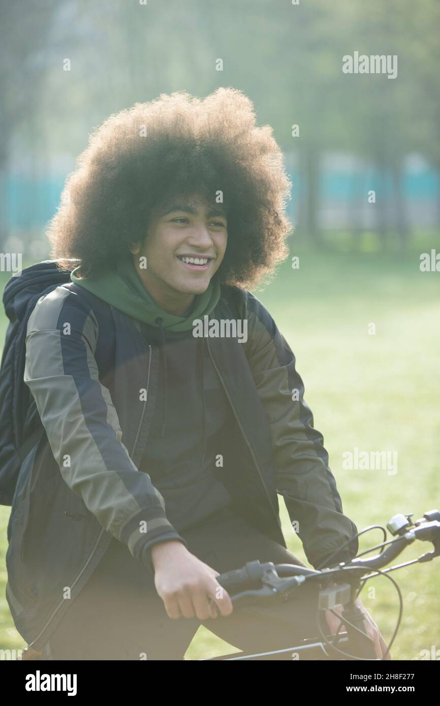 Glücklicher junger Mann mit Afro auf dem Fahrrad im Park Stockfoto
