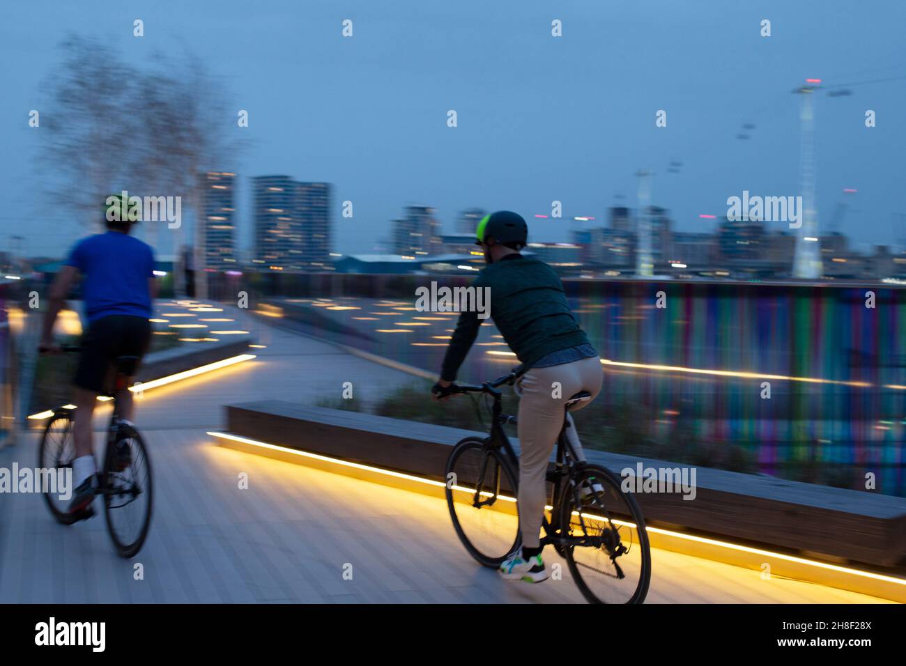 Männer, die nachts auf einer beleuchteten Promenade in der City in London Fahrrad fahren Stockfoto