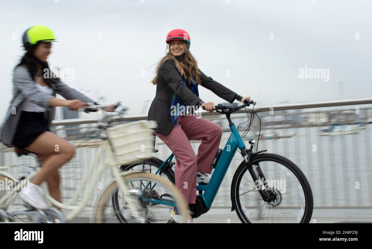 Glückliche junge Freundinnen, die auf der Stadtbrücke Fahrrad fahren Stockfoto
