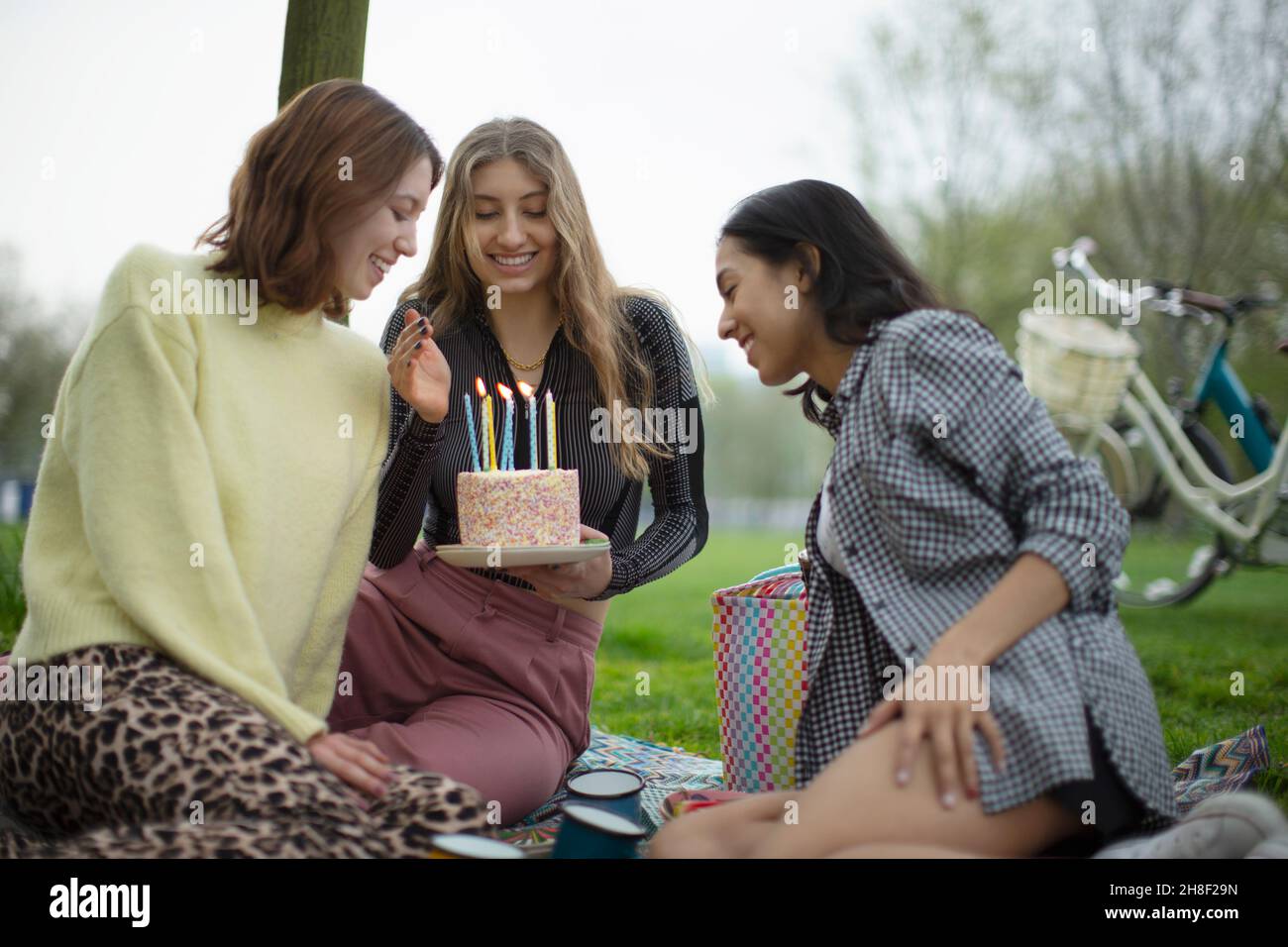 Glückliche junge Freundinnen feiern Geburtstag mit Kuchen im Park Stockfoto