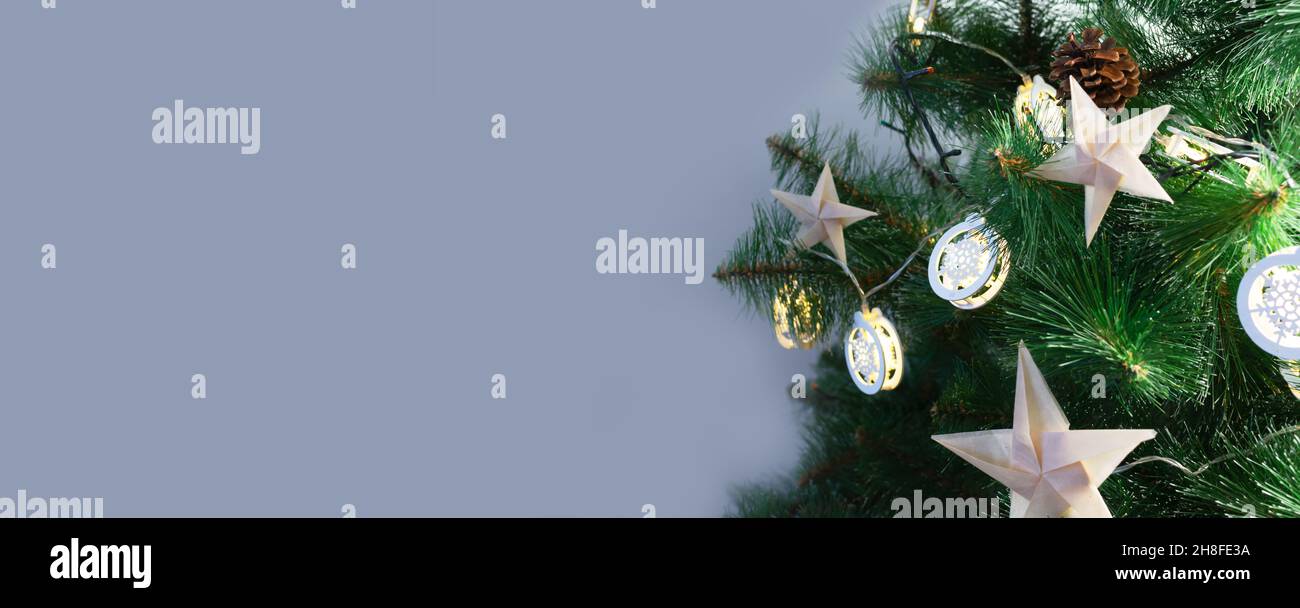 Origami-Sterne aus Bastelpapier auf einem künstlichen Weihnachtsbaum mit festlichen Lichtern auf grauem Hintergrund. Alternative umweltfreundliche Weihnachtsbaum dez Stockfoto