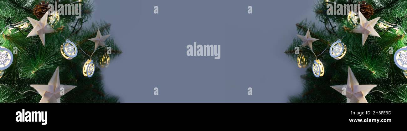 Origami-Sterne aus Bastelpapier auf einem künstlichen Weihnachtsbaum mit festlichen Lichtern auf grauem Hintergrund. Alternative umweltfreundliche Weihnachtsbaum dez Stockfoto