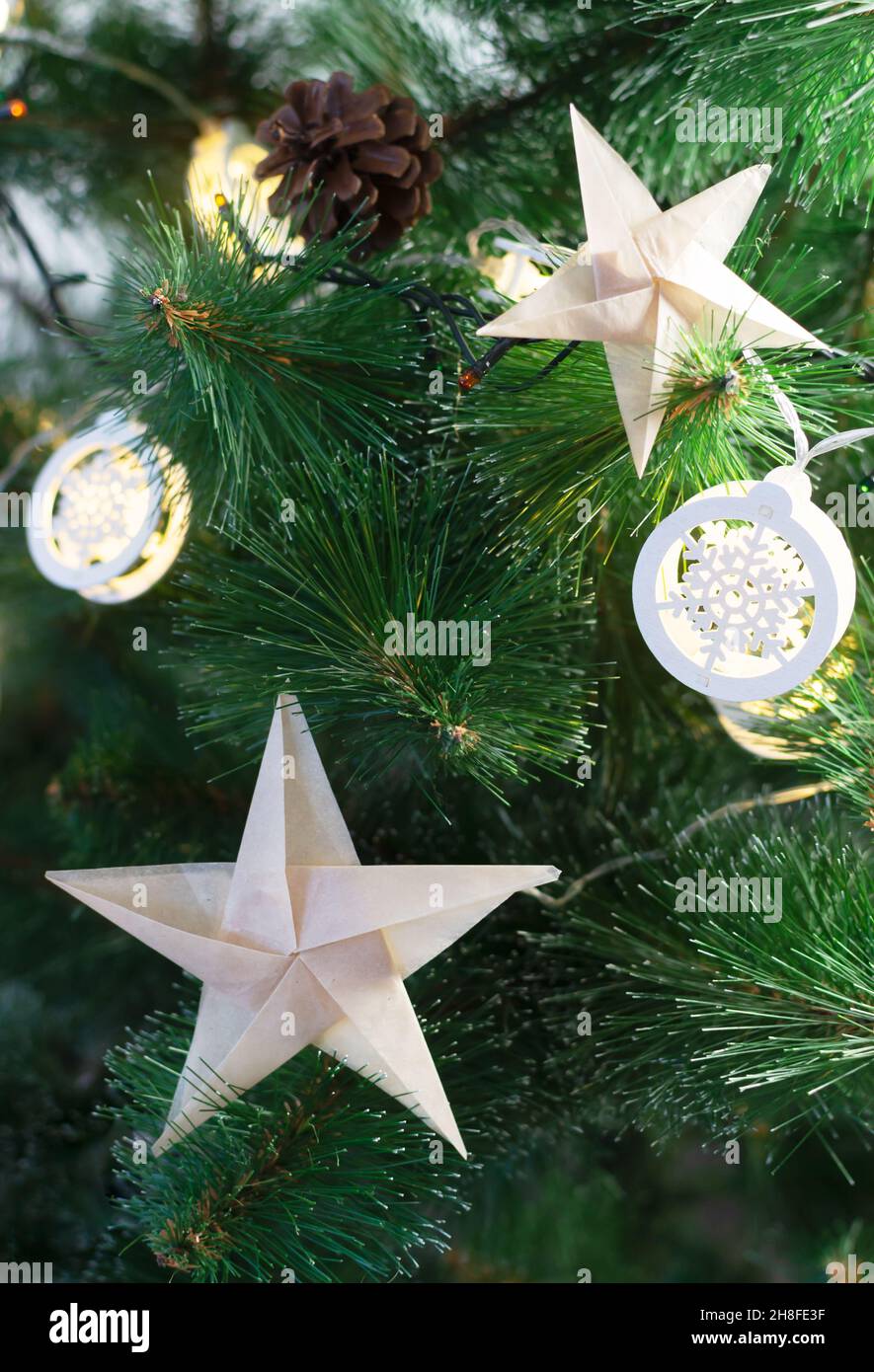 Origami-Sterne aus Bastelpapier auf einem künstlichen Weihnachtsbaum mit festlichen Lichtern. Alternative umweltfreundliche Weihnachtsbaum Dekoration Konzept. DIY. V Stockfoto