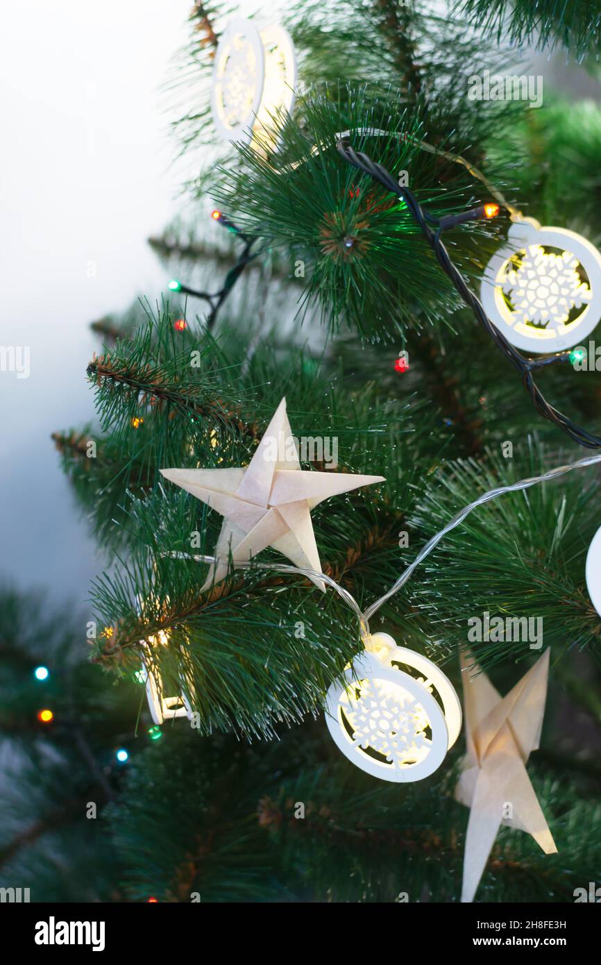 Origami-Sterne aus Bastelpapier auf einem künstlichen Weihnachtsbaum mit festlichen Lichtern. Alternative umweltfreundliche Weihnachtsbaum Dekoration Konzept. DIY. V Stockfoto