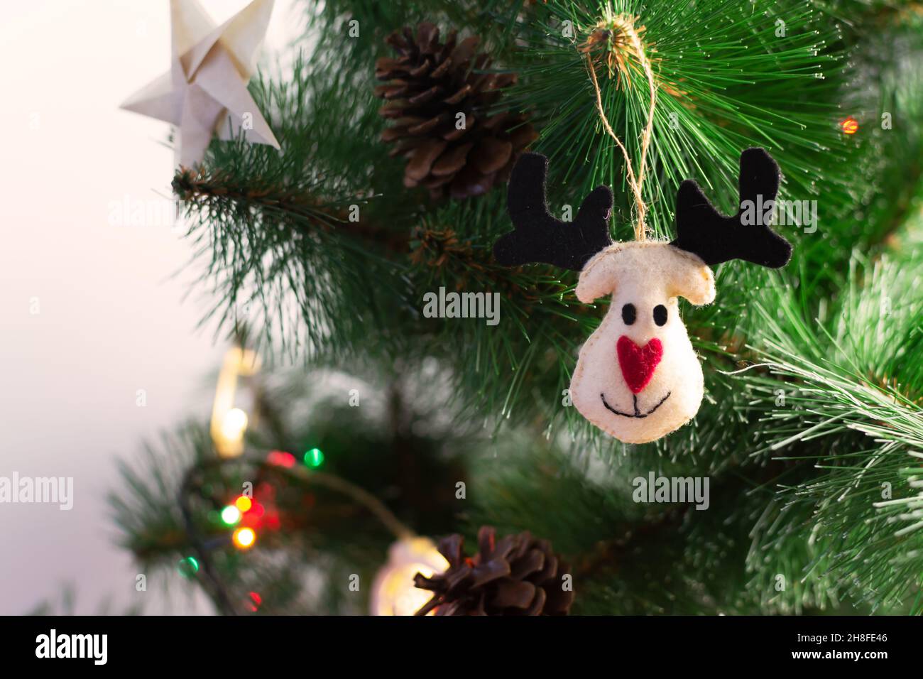 Filzspielzeug Weihnachtshirsch mit Origami-Sternen auf einem künstlichen Weihnachtsbaum mit festlichen Lichtern. Umweltfreundliches Konzept. Alternative Weihnachtsspielzeuge. Hori Stockfoto