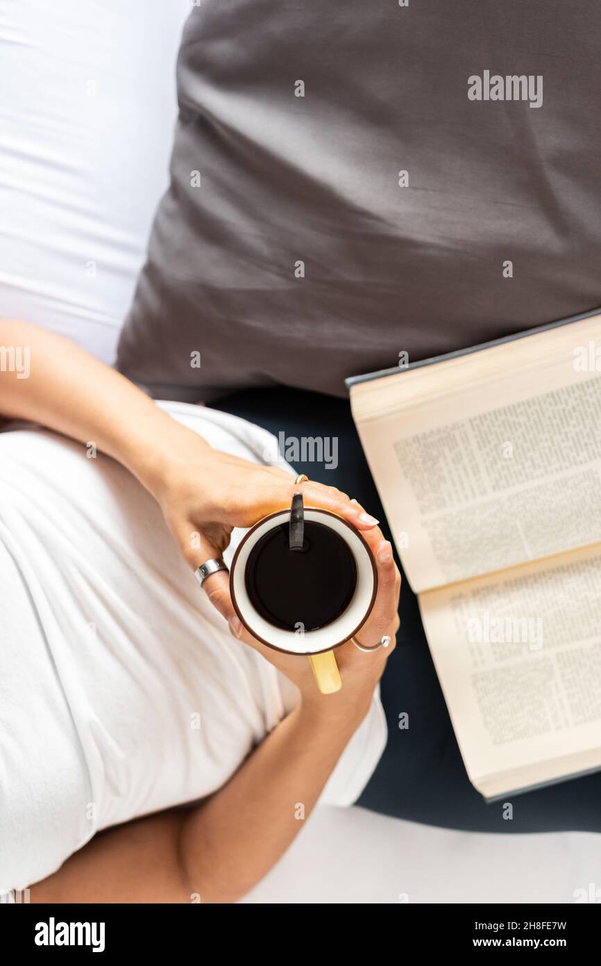 Mädchen liegt im Bett mit einer Tasse Kaffee in den Händen und einem Buch Stockfoto