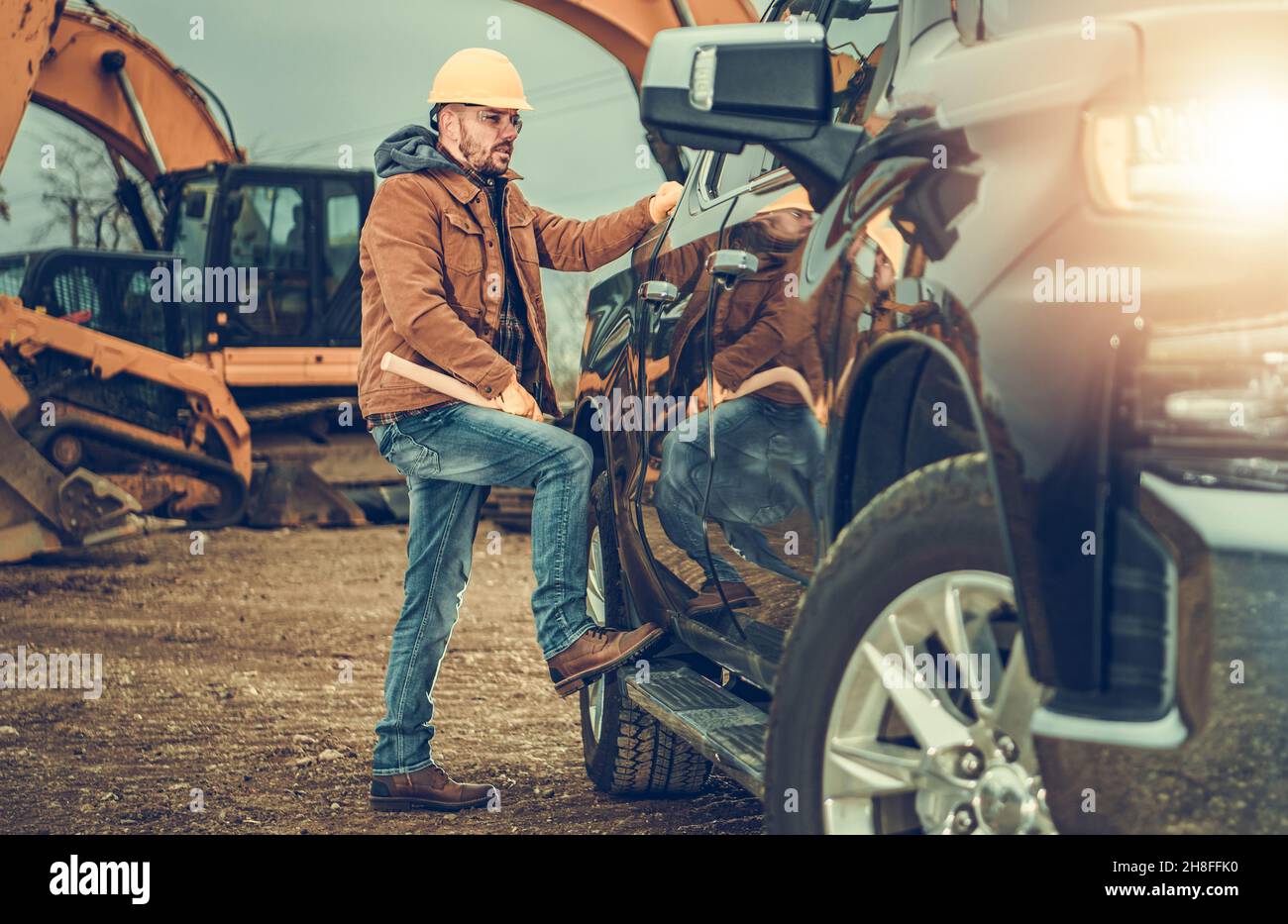 Bau- und Schwerbodenmaschinen-Geschäftsinhaber neben seinem Pickup Truck. Bagger im Hintergrund. Stockfoto