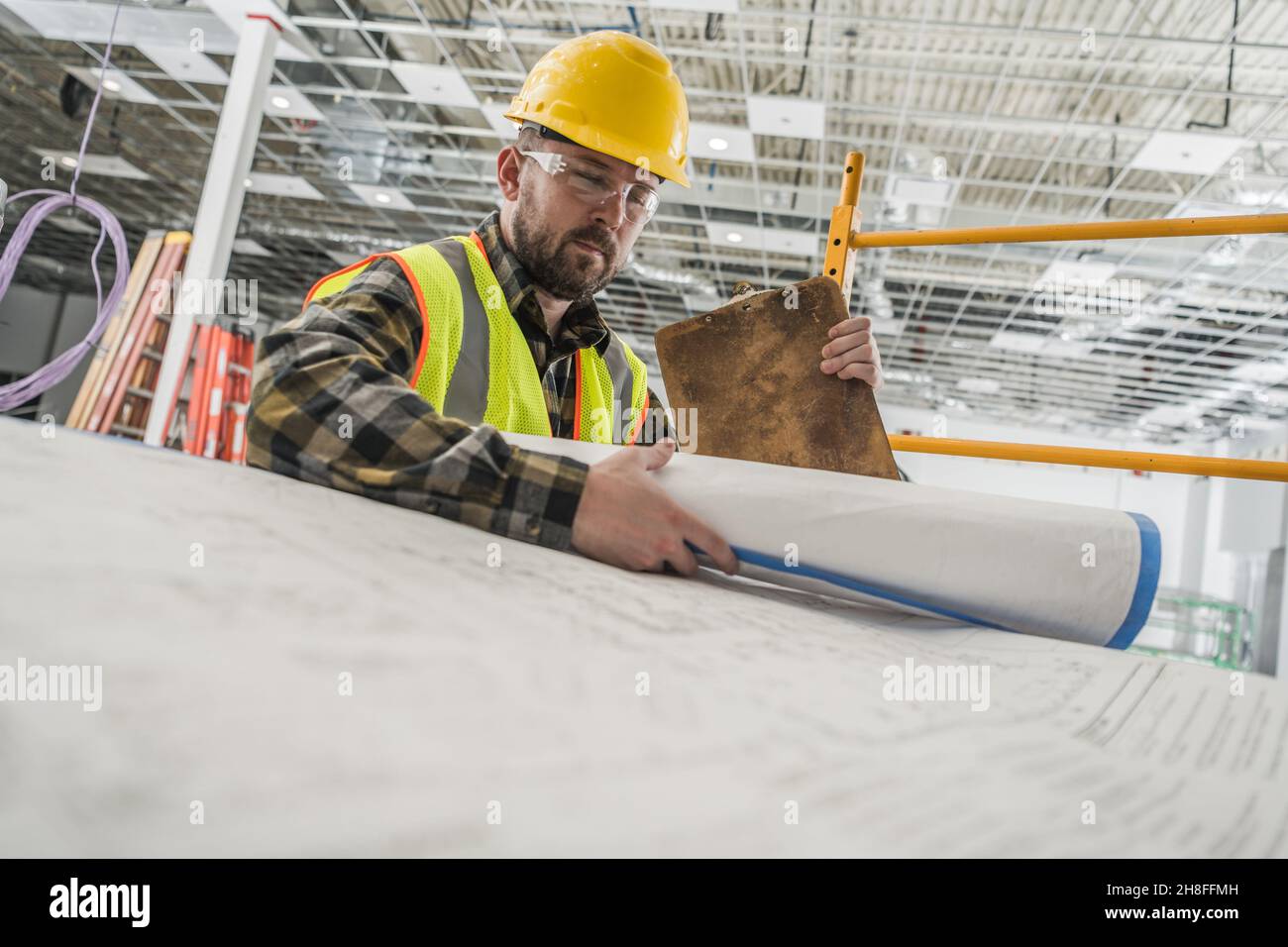 Bauunternehmer Arbeiter in seinem 30s Blick in große Papiergebäude Blueprints. Thema Bauindustrie. Stockfoto