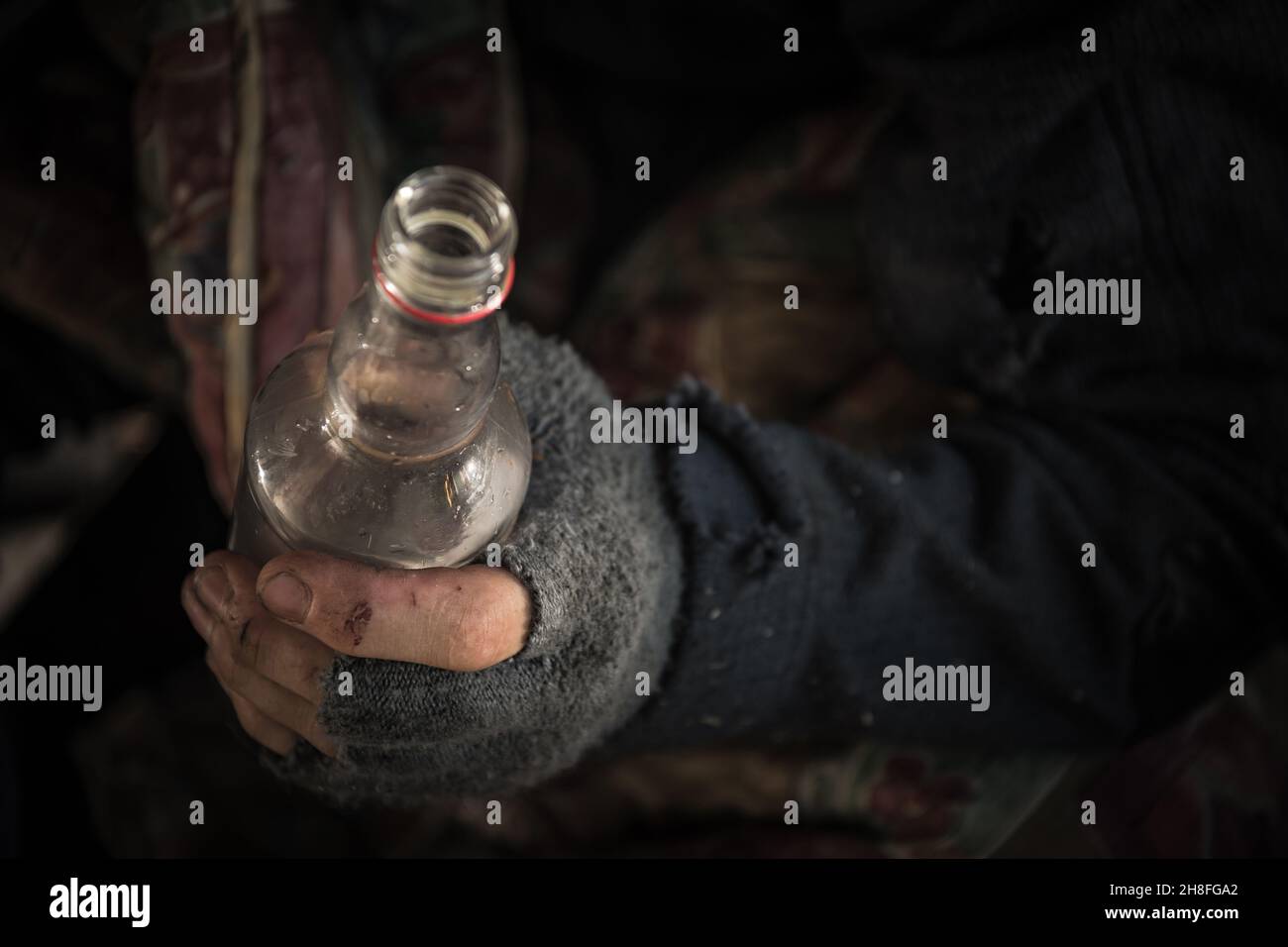 Kaukasische Obdachlose Männer tragen fingerlose Handschuhe mit einer Flasche Vodka aus nächster Nähe. Stockfoto