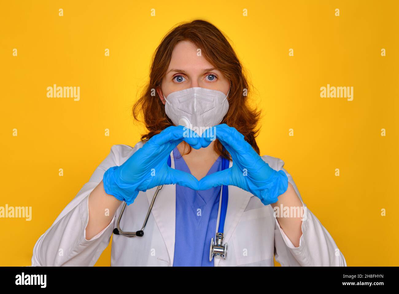 Der Arzt zeigt ein Herzzeichen in Schutzhandschuhen, Nahaufnahme. Hände eines Sanitäter in einer Uniform mit einem Zeichen der Liebe zu Patienten mit Coronavirus, Konzept Stockfoto