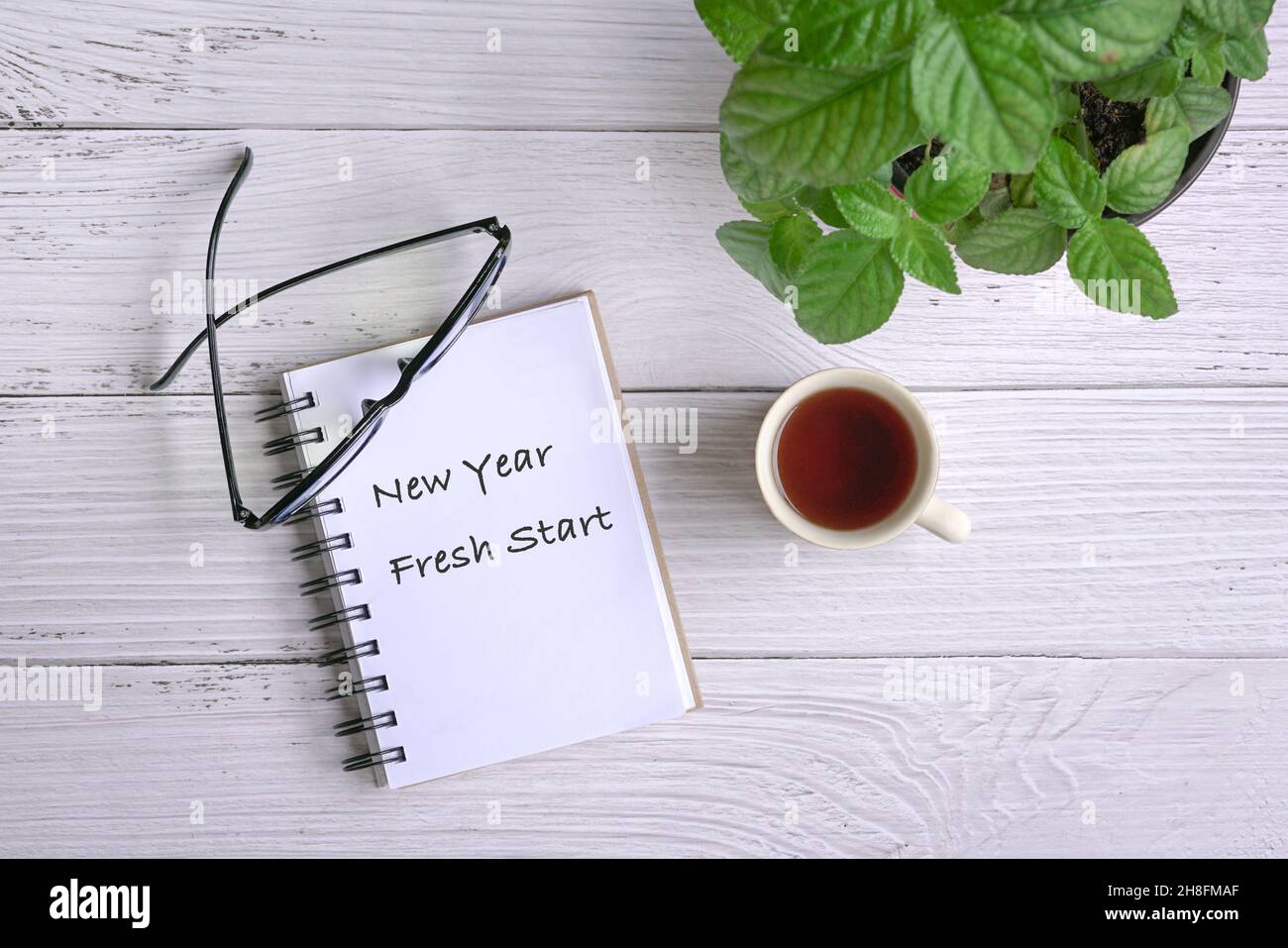 Notizblock mit Text, Neujahr Fresh Start, mit Kaffee, Brille und grüner Pflanze auf dem Tisch. Draufsicht. Stockfoto