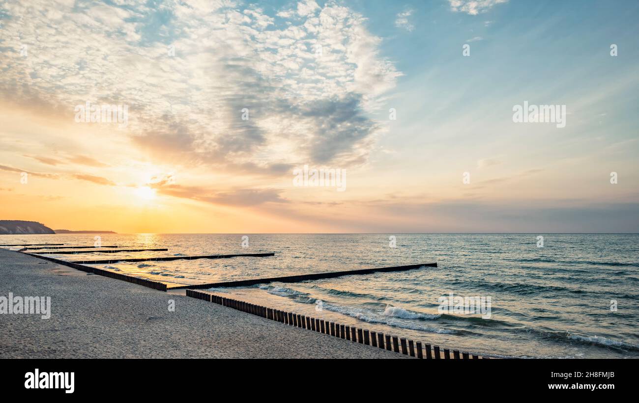 Panorama des Abendmeeres mit einem hölzernen Wellenbrecher am Sandstrand vor dem Hintergrund des Sonnenuntergangs Stockfoto