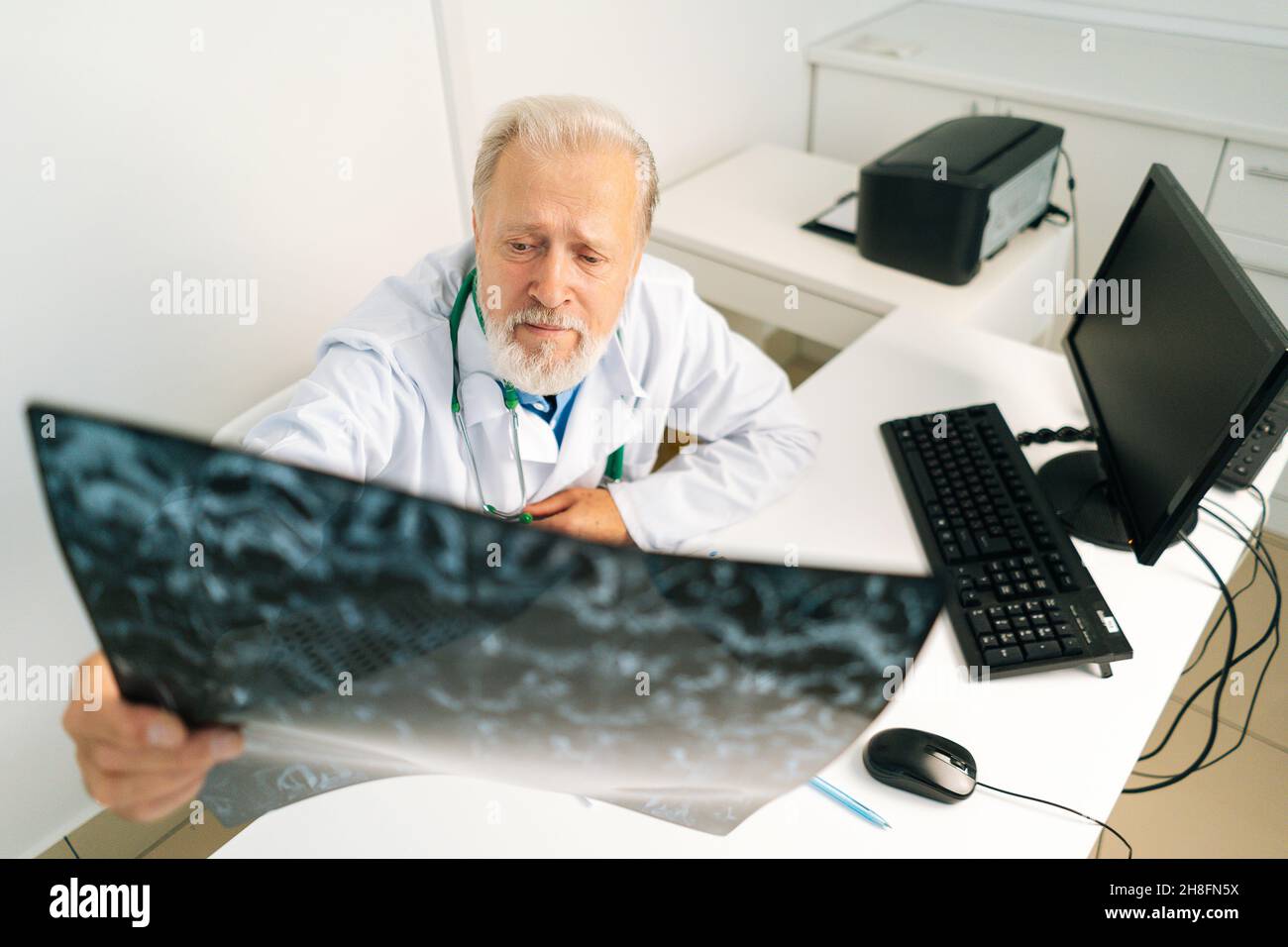 Aus der Perspektive eines erwachsenen Arztes, der die MRT-Wirbelsäulenaufnahme eines Patienten untersucht, der am Schreibtisch mit Computer im medizinischen Büroraum sitzt. Stockfoto
