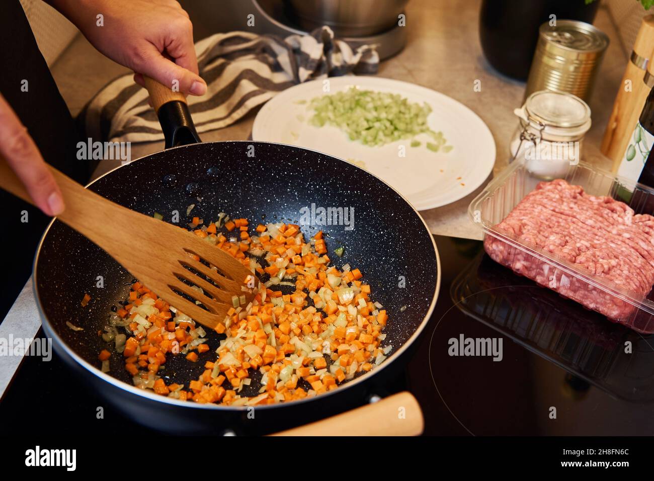 Frau kocht Bolognese-Sauce in der Pfanne auf Induktionsherd in der Küche Stockfoto
