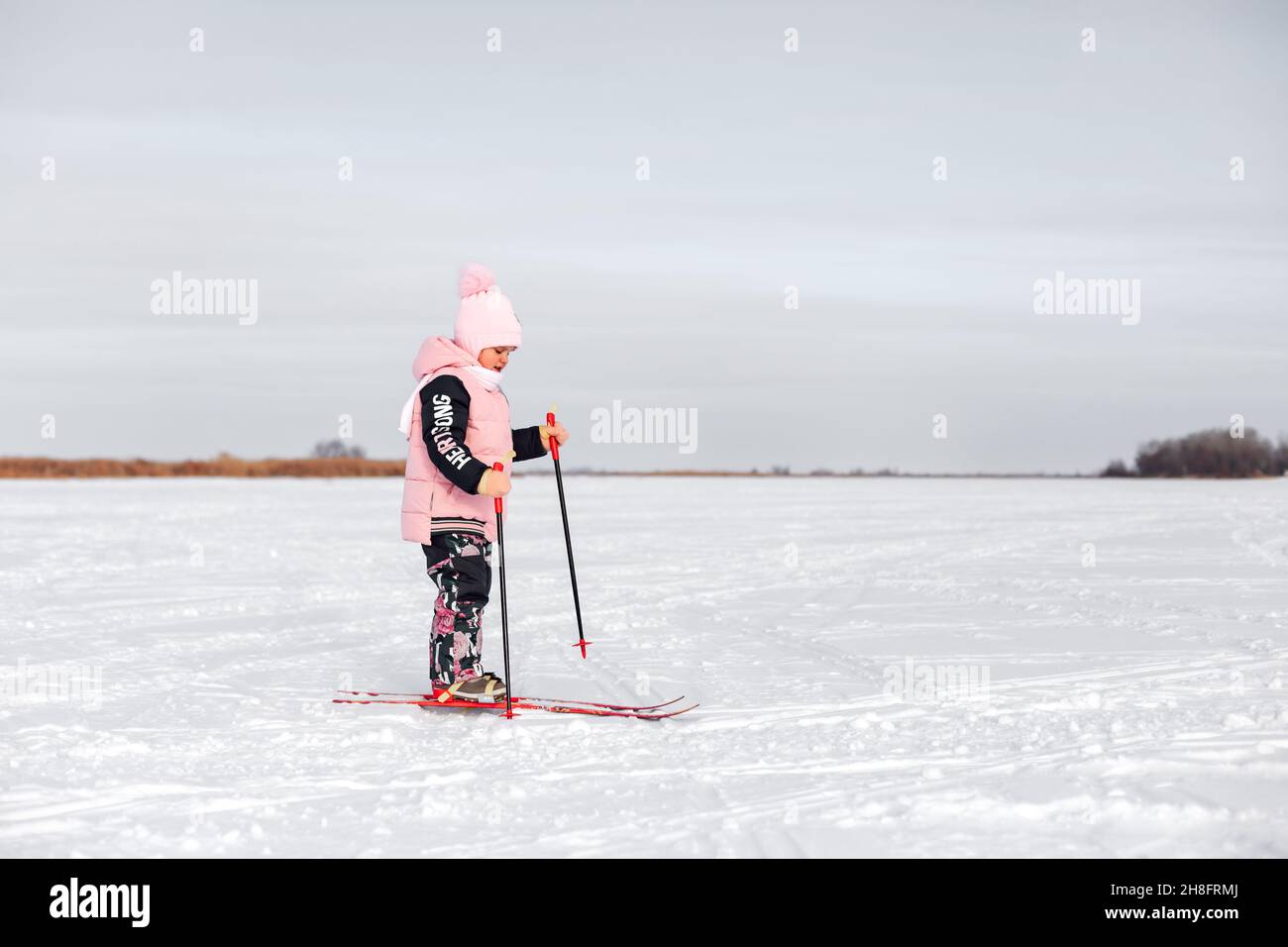 Das kleine Mädchen lernt Skifahren. Kind in rosa warmen Anzug Skifahren im Schnee am frostigen Wintertag, Seitenansicht, Schnee Hintergrund Stockfoto