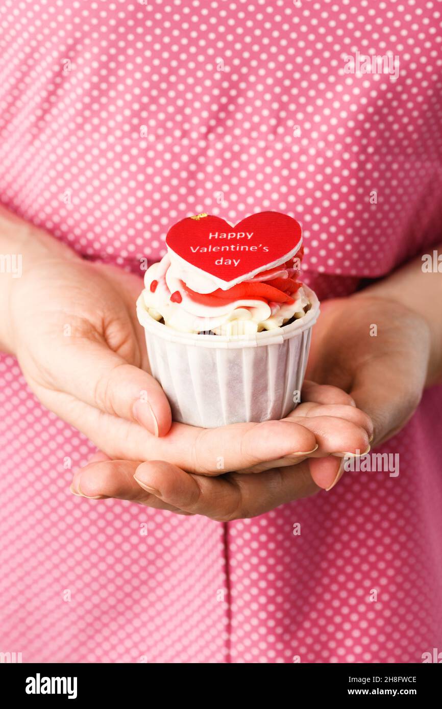 Geformter Herzkuchen in den Händen mit der Aufschrift Happy Valentine's Day auf rosa Hintergrund. Cupcake in Form von Herz-Nahaufnahme Stockfoto