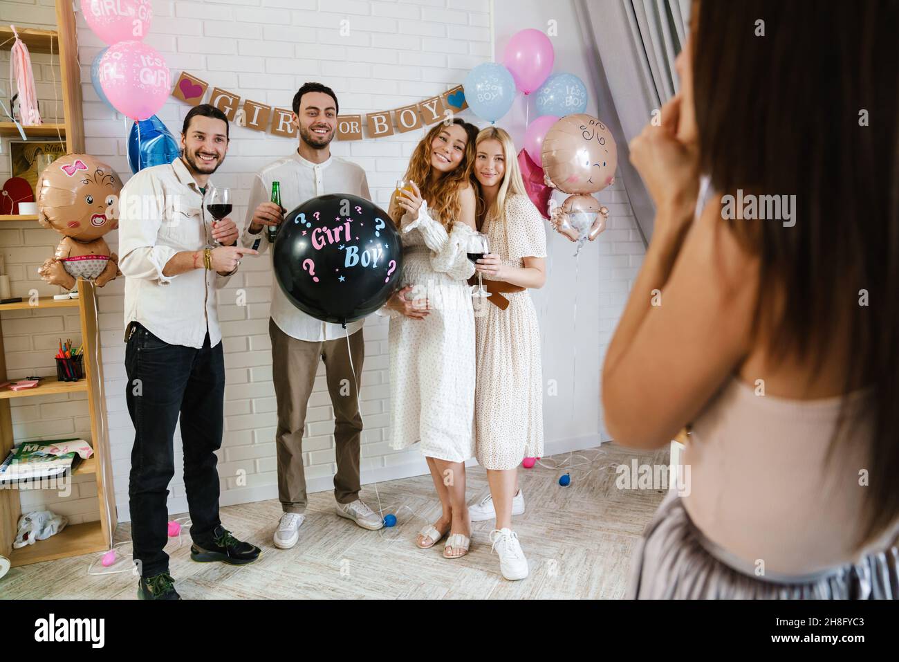 Eine Gruppe von glücklichen Freunden bei einem Geschlecht enthüllt eine Babydusche, hält einen Ballon und macht ein Foto von einem Fotografen Stockfoto