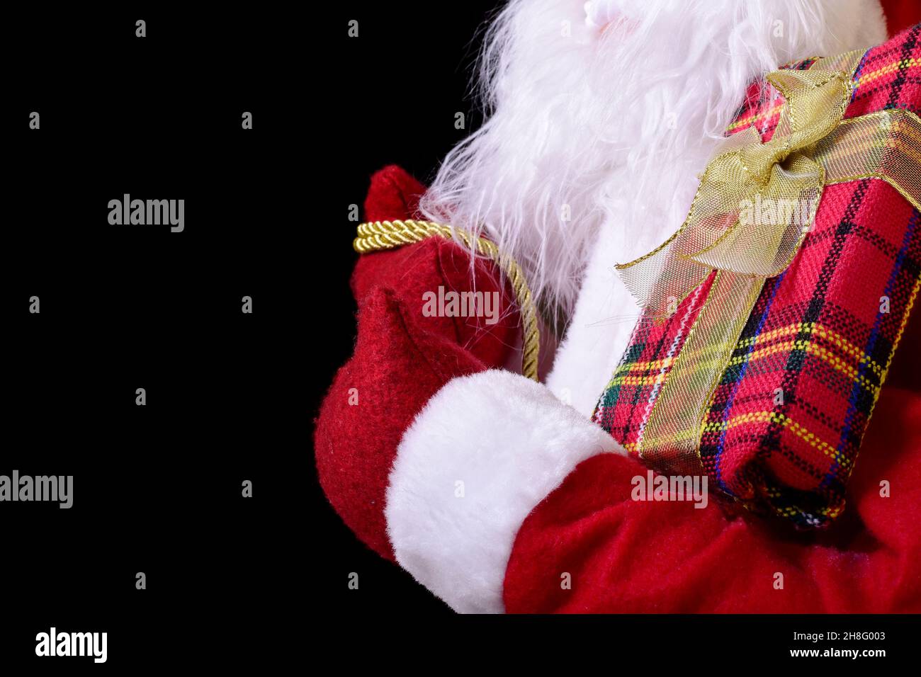 Foto eines roten Geschenkpakets auf dem Arm des Weihnachtsmanns. Das Foto hat einen großen Kopierbereich und einen schwarzen Hintergrund. Stockfoto