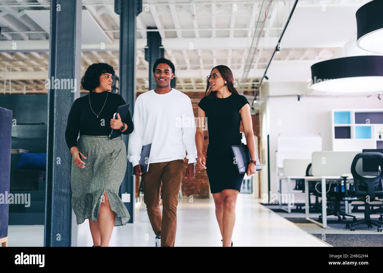 Geschäftsleute unterwegs. Gruppe von drei selbstbewussten Geschäftsleuten, die miteinander sprechen, während sie gemeinsam in einem modernen Büro spazieren. Kollegen arbeiten Stockfoto