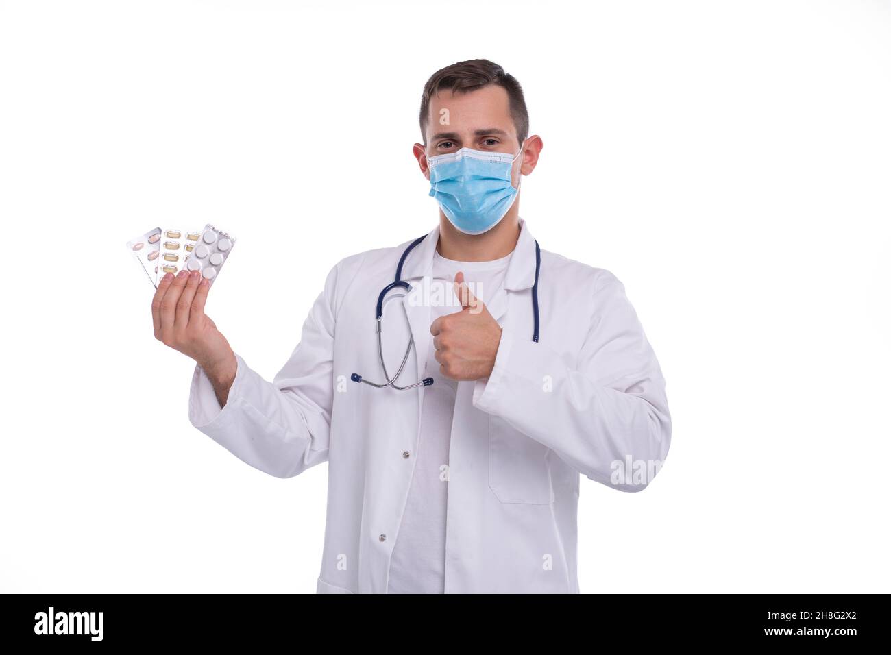 Mann Arzt zeigt Pillen und Daumen nach oben trägt medizinische Maske. Doctor Holding Tablets. Mann, Doktor, Isoliert. Stockfoto