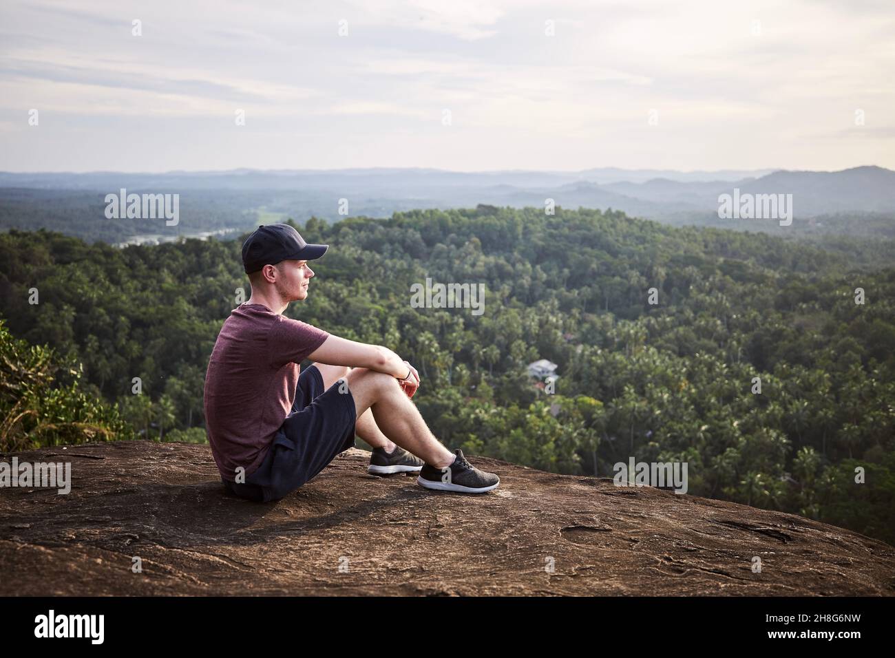 Nachdenklicher Mann, der sich am Rand eines Felsens ausruht und die Aussicht anschaut. Landschaft mit tropischem Regenwald in Sri Lanka. Stockfoto