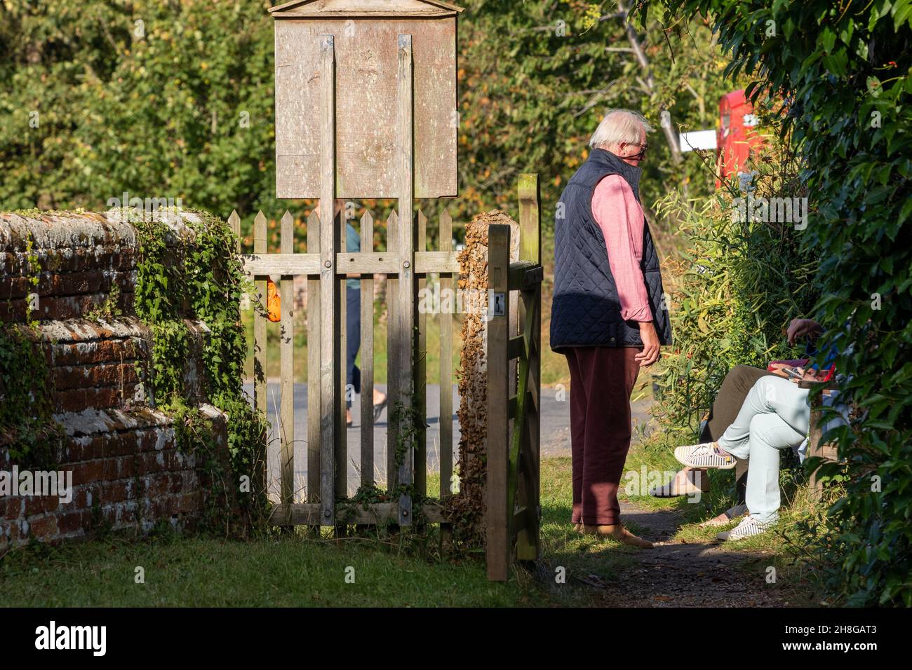 Im Landhausstil gekleideter Mann führt ein Gespräch mit zwei nahezu unsichtbaren sitzenden Frauen Stockfoto