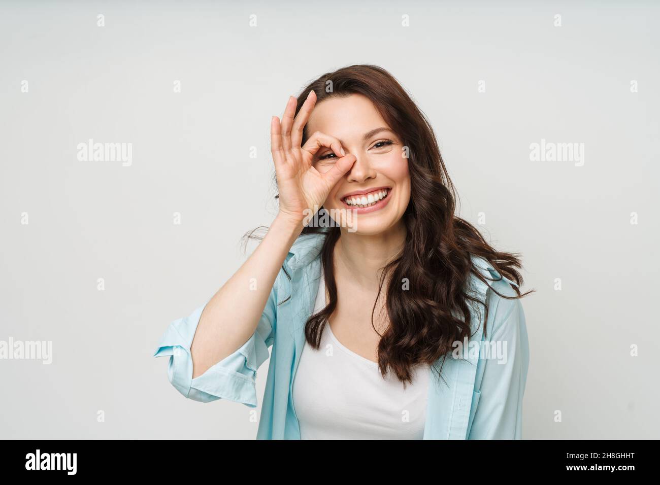 Porträt einer lächelnden Frau, die ein OK-Zeichen zeigt und in eine isolierte Kamera auf weißem Hintergrund blickt. Stockfoto
