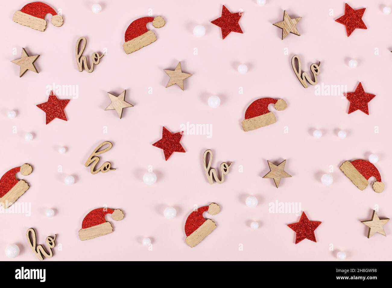 Weihnachtsdekorationen in Form von weihnachtsmützen, Schneebällen und Textornamenten mit der Aufschrift „ho ho ho ho“ auf rosa Hintergrund Stockfoto