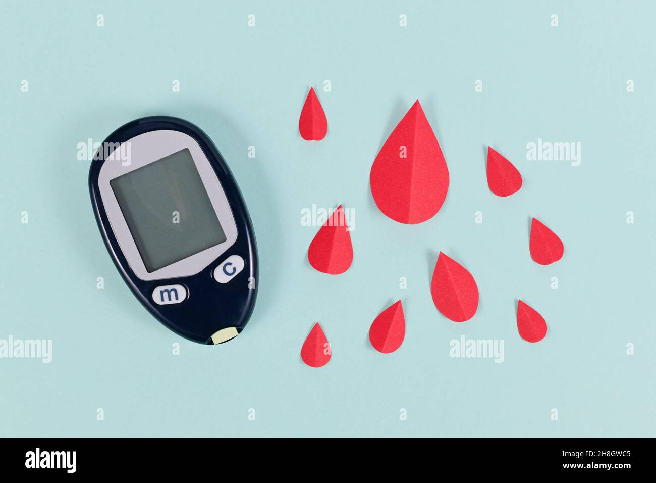 Blutzucker-Messgerät für Diabetes-Erkrankungen neben Papierbluttropfen Stockfoto