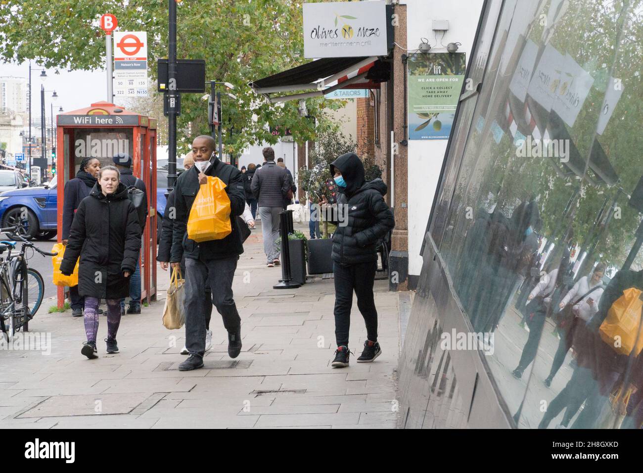 London, Großbritannien, 30. November 2021: Käufer sind nun gesetzlich verpflichtet, in Geschäften oder öffentlichen Verkehrsmitteln eine Gesichtsmaske zu tragen. In der Clapham High Street Filiale des Sainsbury's Supermarkts kommen und gehen die Käufer und entfernen oft ihre Masken, sobald sie draußen an die frische Luft treten. Anna Watson/Alamy Live News Stockfoto