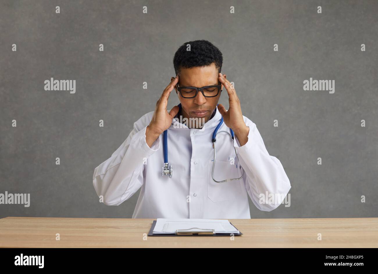 Junger afroamerikanischer Arzt, der an Kopfschmerzen leidet und am Schreibtisch sitzt Stockfoto