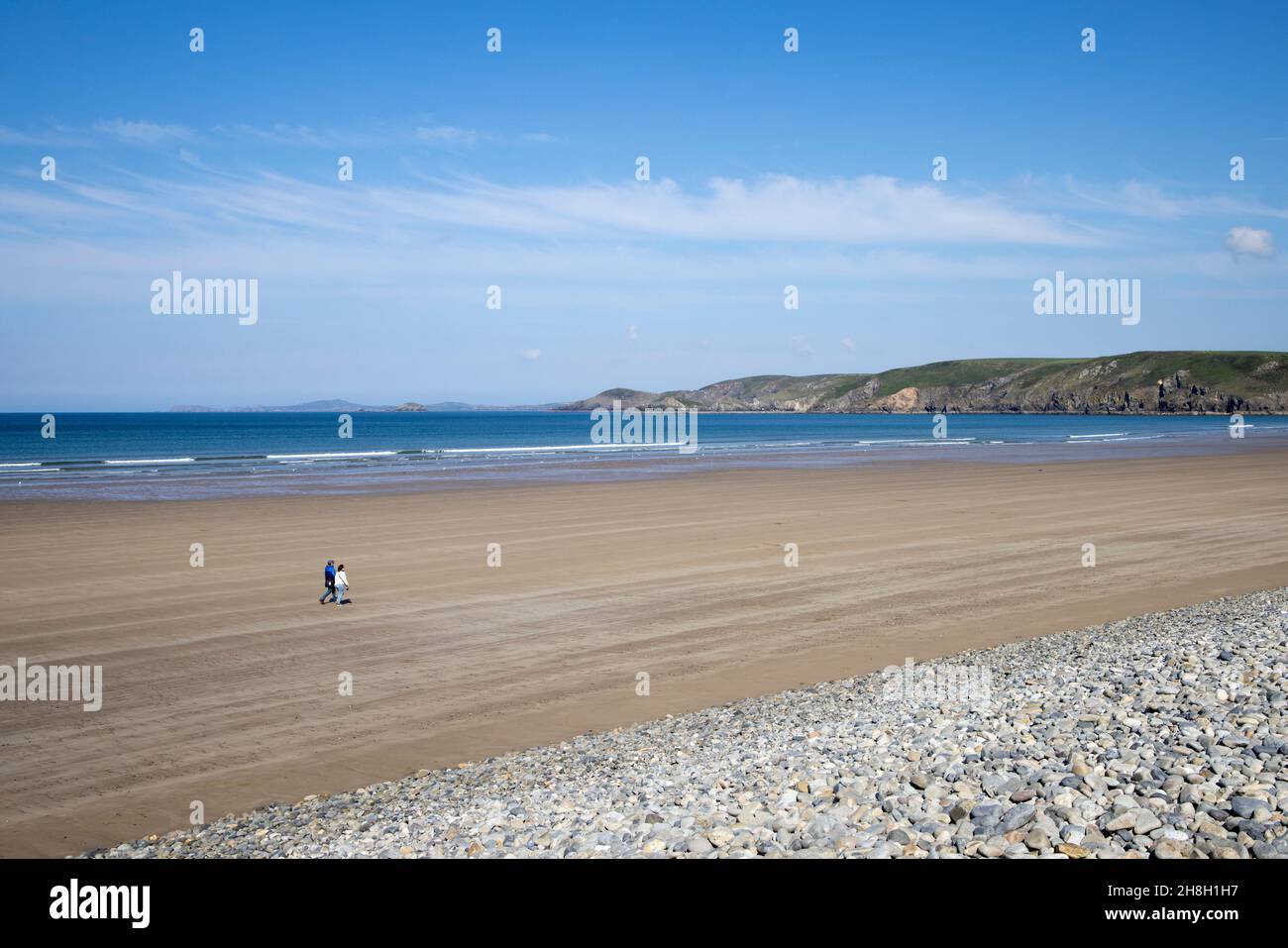 Mann und Frau, die am leeren Strand von Newgale, Pembrokeshire, Wales, Großbritannien, spazieren gehen Stockfoto
