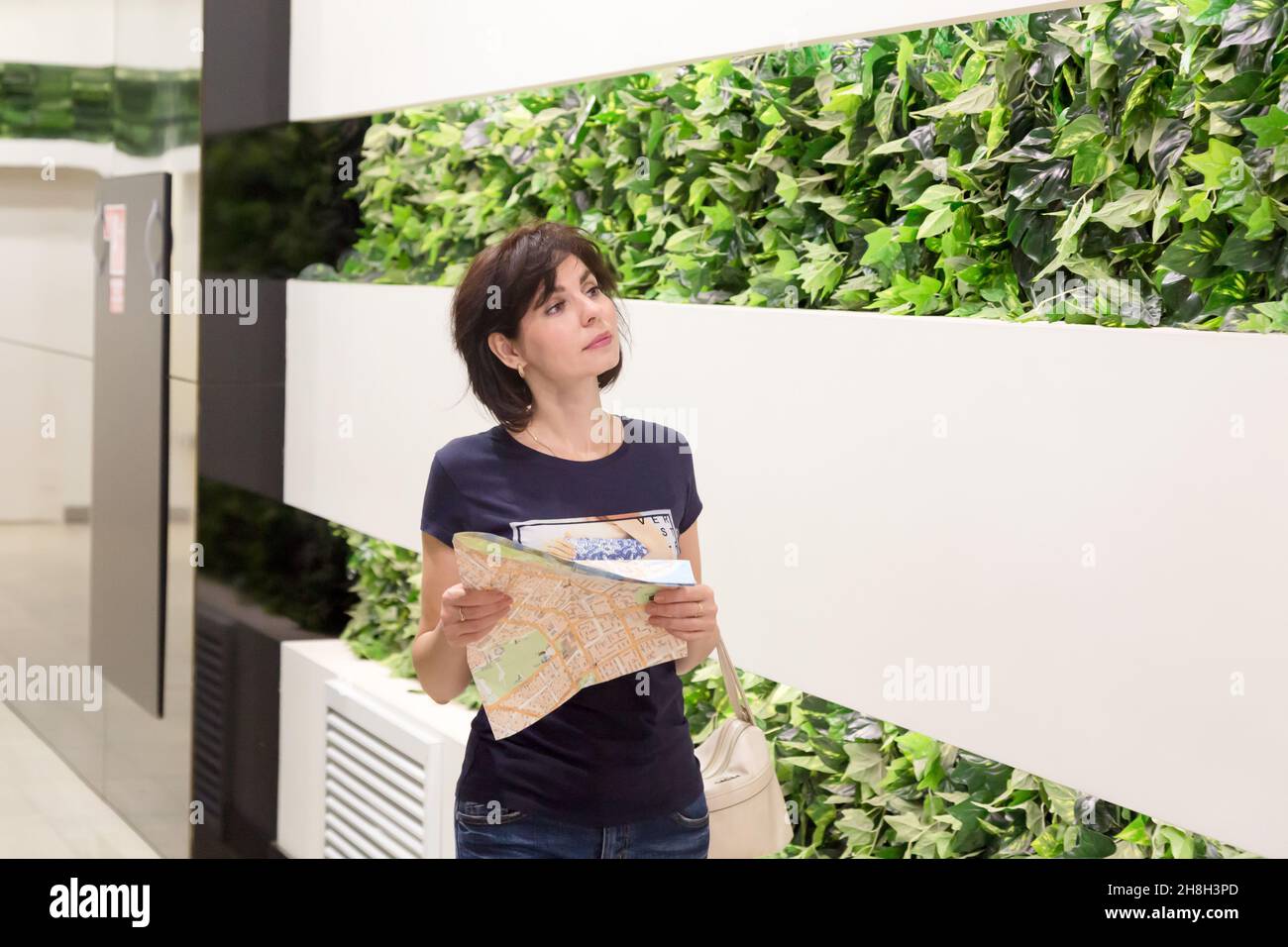 Eine Kundin mit einer Zeichnung in den Händen sucht nach dem richtigen Laden in einem riesigen Einkaufszentrum. Stockfoto