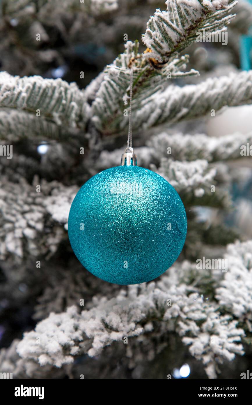 An einem frostigen Weihnachtsbaum hängt eine türkisblaue Glitzerkugel Stockfoto