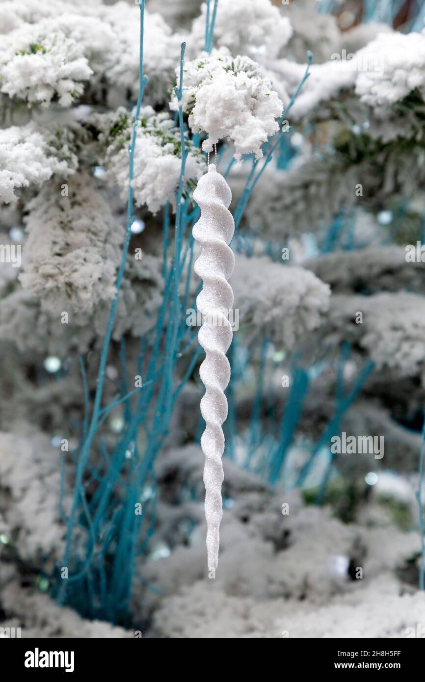 Eikelförmige weiße, glitzernde Kugel, die auf einem schneebedeckten Weihnachtsbaum hängt Stockfoto