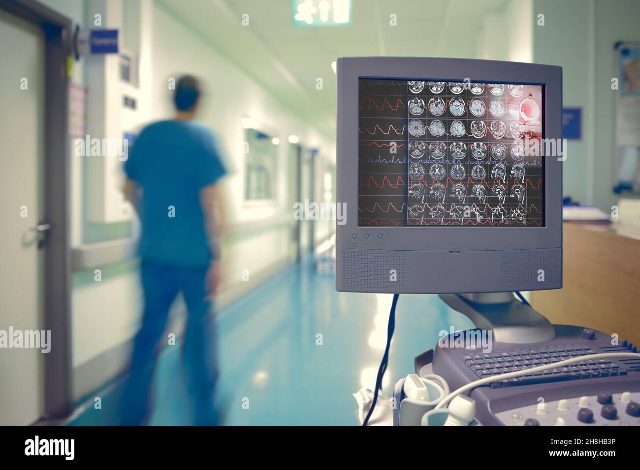 Medizinischer Monitor mit EKG und Hirnscan vor dem Hintergrund einer verschwommenen Silhouette eines männlichen Arztes, der durch den Krankenhausflur geht. Stockfoto