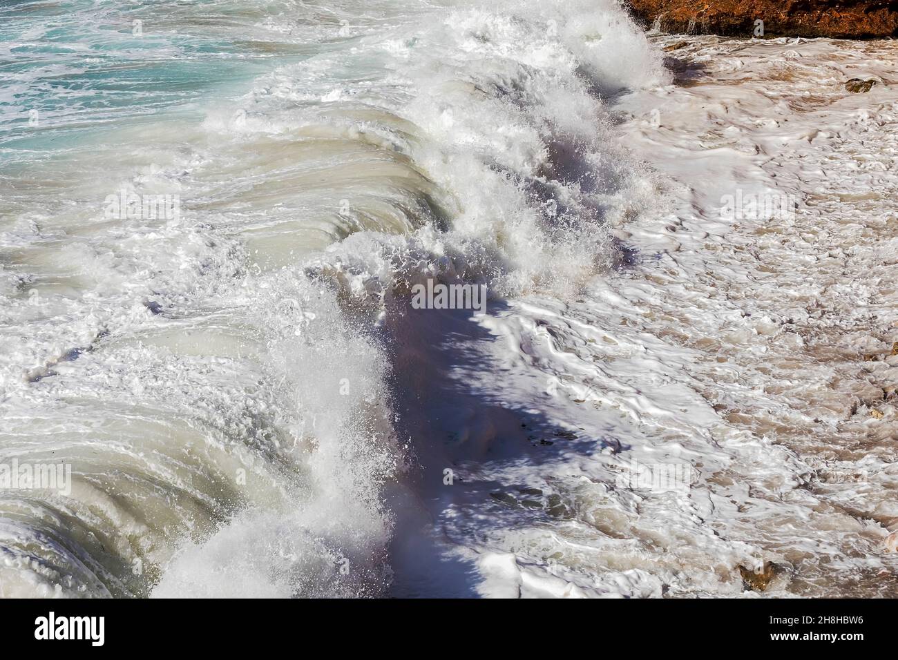 Seafoam mit Wellen, die mit weißem milchigem Spray auf das Ufer treffen. Stockbild. Stockfoto