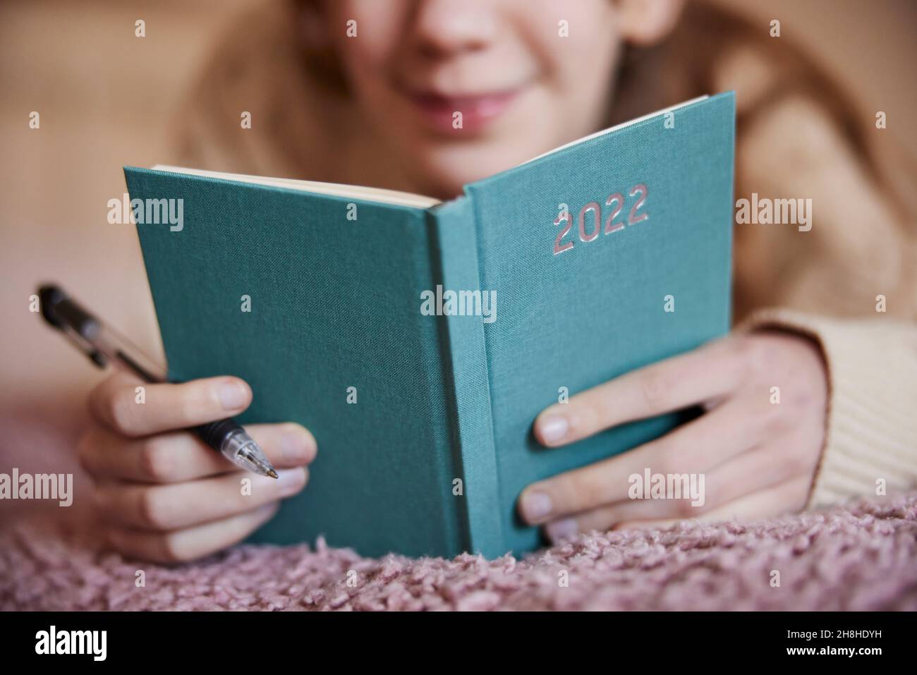 Nahaufnahme Des Teenage-Mädchens, Das Zu Hause Auf Dem Bett Liegt Und Vorsätze Im Neujahrs-Tagebuch 2022 Schreibt Stockfoto