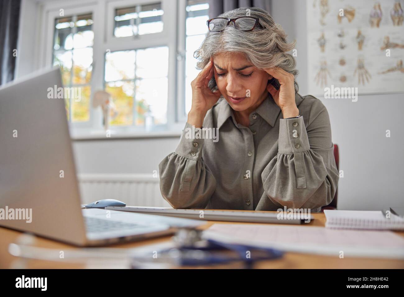 Gestresster und überarbeiteter reifer Hausarzt am Schreibtisch im Ärztebüro Stockfoto