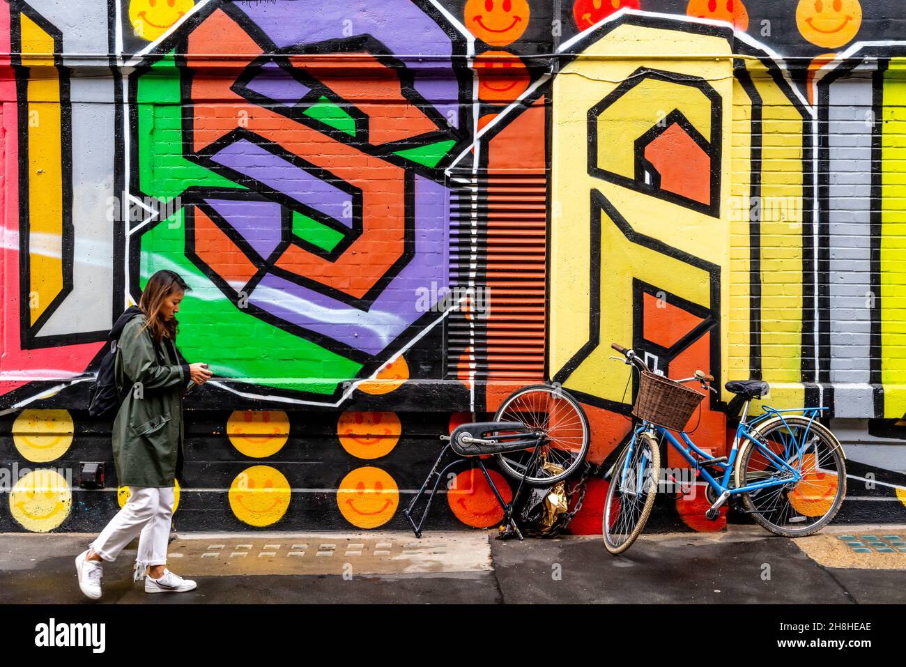 Eine junge Frau geht an einigen Street Art/Graffiti vorbei, Shoreditch, London, Großbritannien. Stockfoto