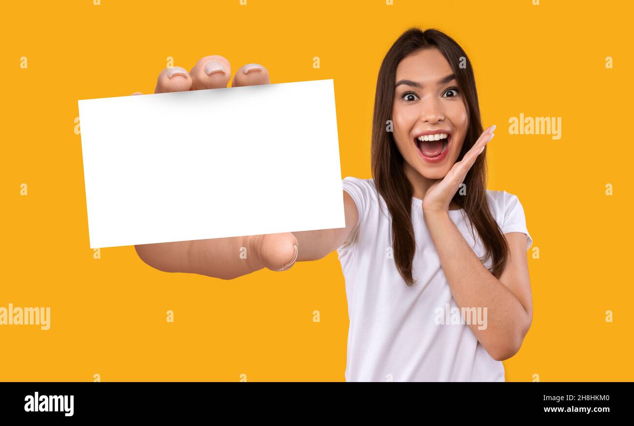 Porträt einer aufgeregten jungen kaukasischen Frau, die eine leere weiße Papierkarte mit Mockup für Ihre Geschäftsinformationen hält Stockfoto