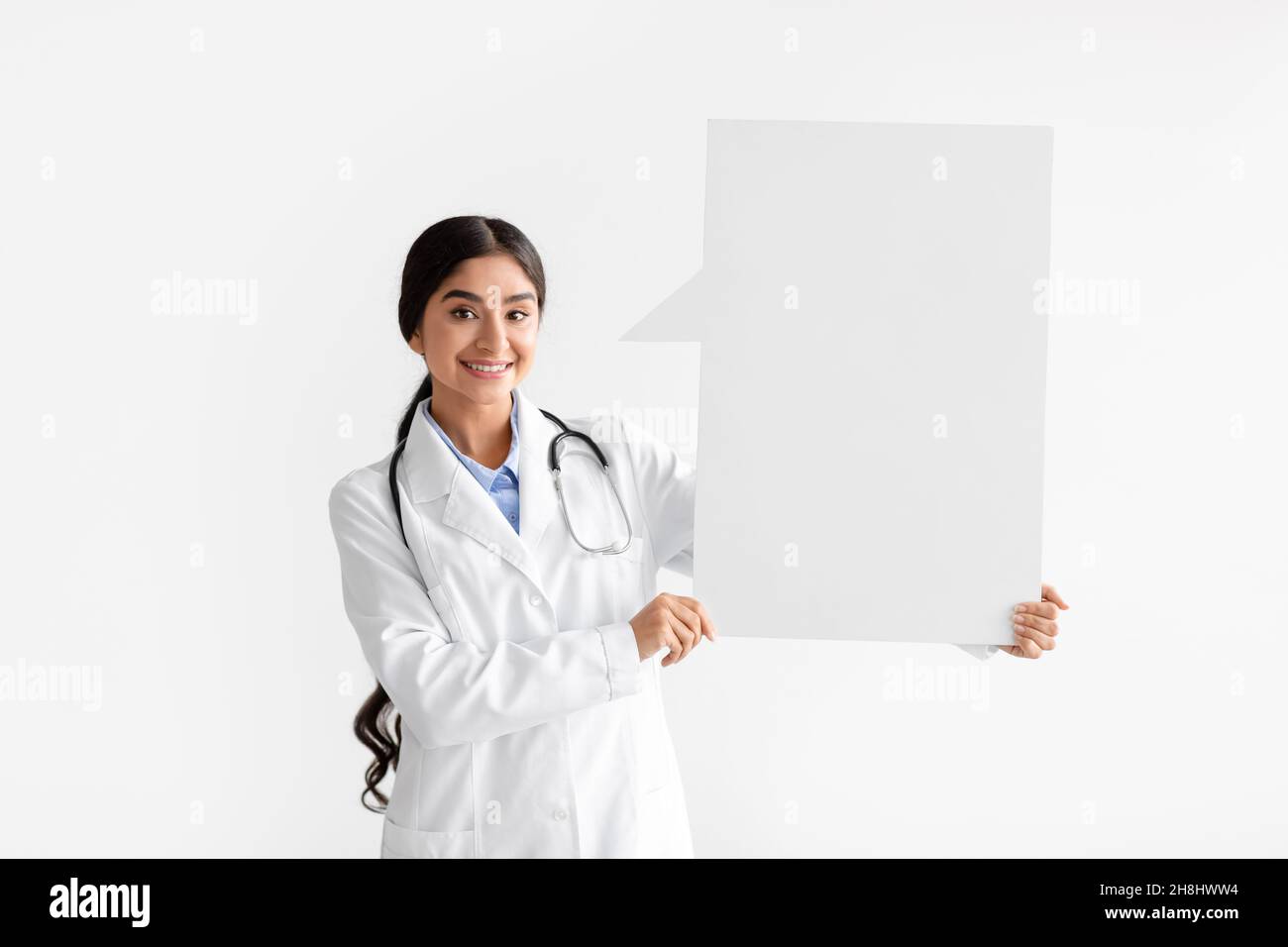 Fröhliche junge hindu-Ärztin im weißen Mantel hält abstrakten Raum für Worte und Gedanken mit leeren Raum Stockfoto