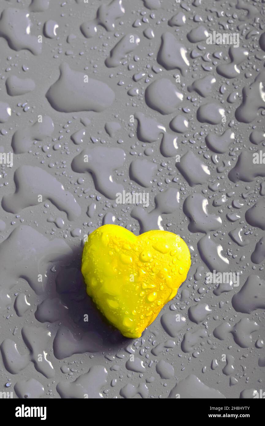 Gelbes Herz mit grauem Hintergrund und Wassertropfen wie romantischer Hintergrund Stockfoto