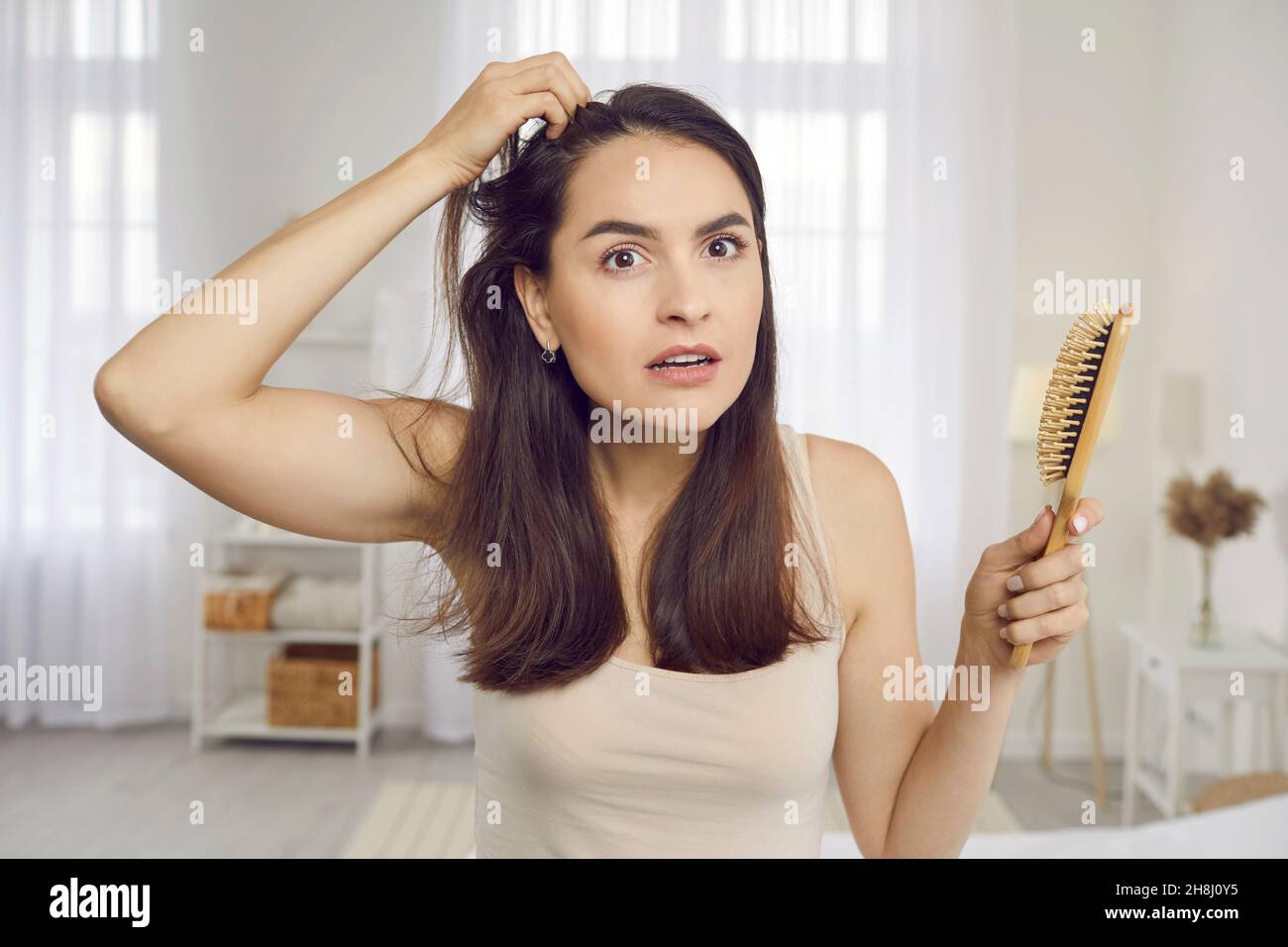 Unglückliche junge Frau, die Schuppen auf ihrer Kopfhaut ansieht oder Anzeichen von Haarausfall bemerkt Stockfoto