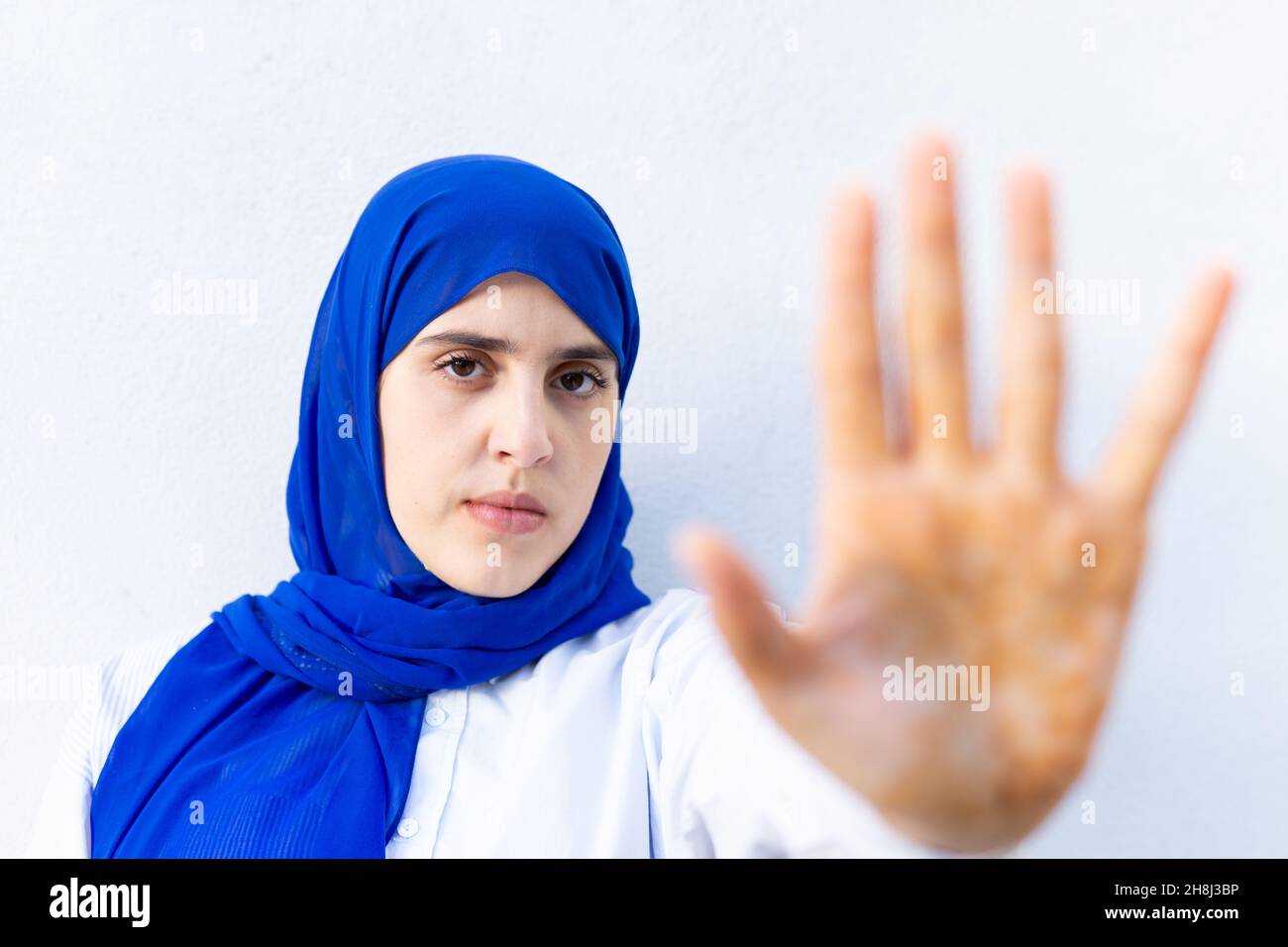 Junge muslimische Frau mit Hijab, die die Kamera anschaut und dabei eine Stoppgeste macht Stockfoto