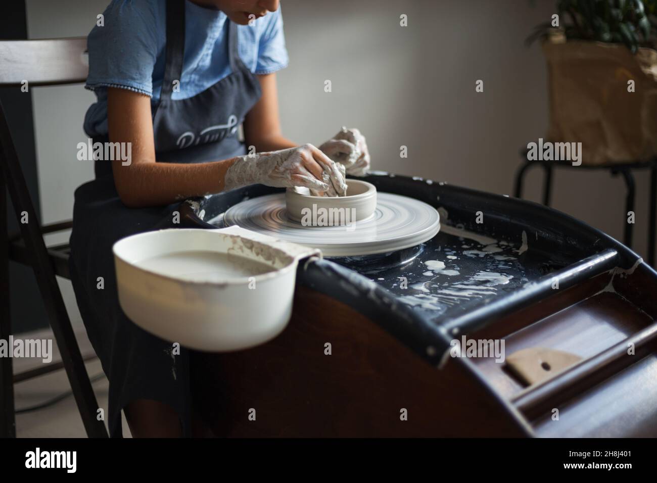 Hände des Mädchens, die einen Topf auf dem Töpferrad erschaffen. Traditionelles Handwerk. Meisterkurs zur Modellierung von Ton auf einem Töpferrad in der Töpferwerkstatt. Erstellen Stockfoto